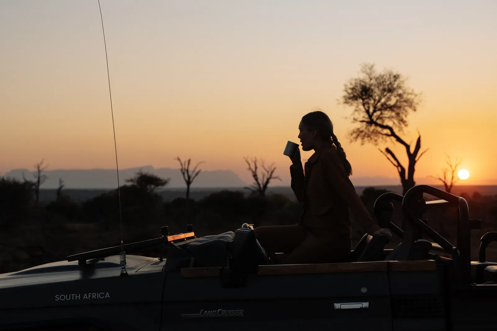 Chloe's silhouette at dusk, drinking coffee on the back of a safari truck