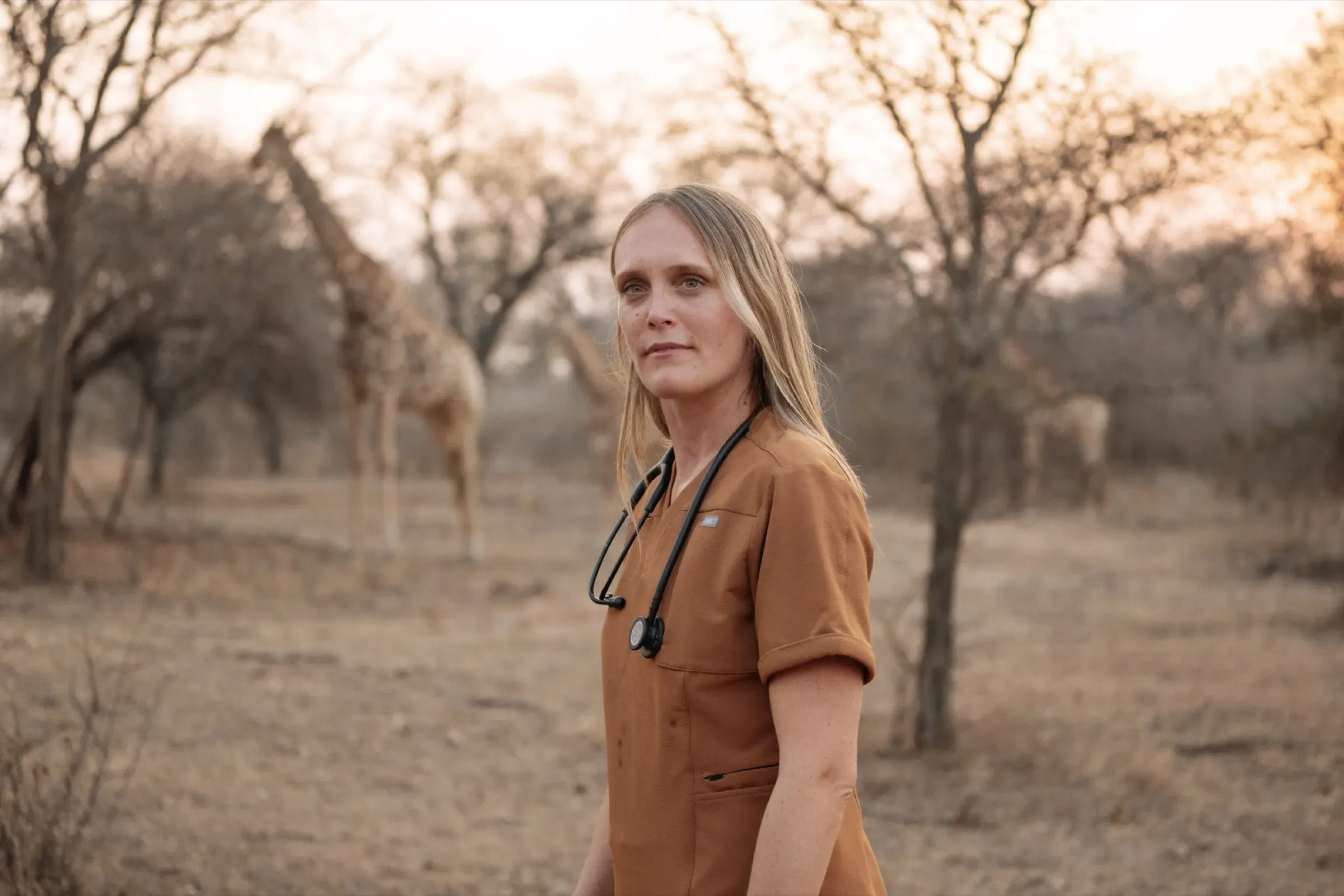Dr Chloe Buiting in the field at sunset, with giraffes behind her