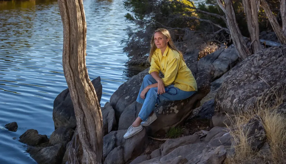 Dr Chloe Buiting sitting on rocks by a river